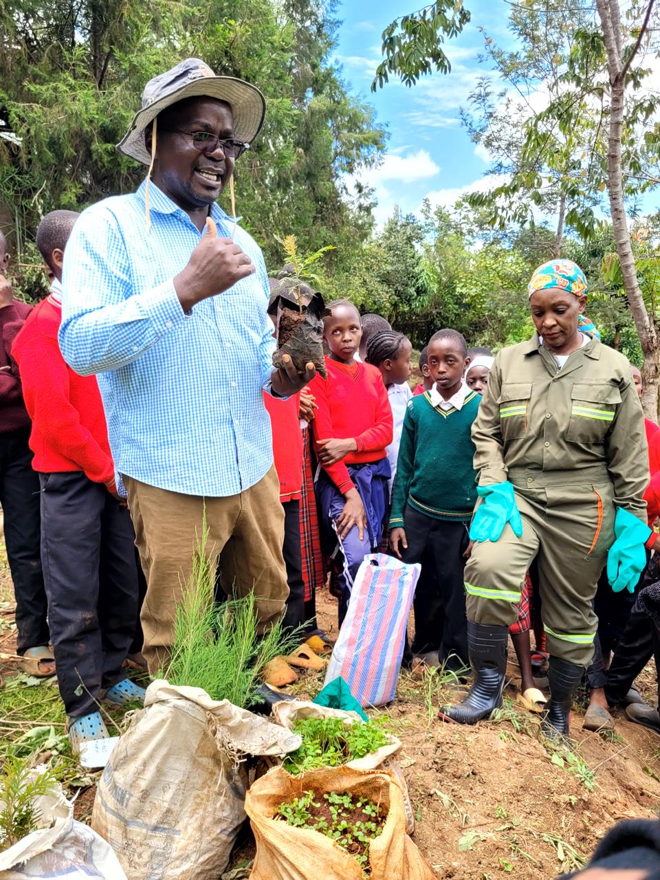 A trainer demonstrating tree seedling planting to pupils